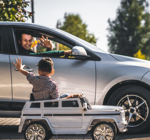 child in a toy car waving to an adult in a real car